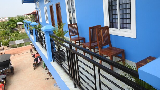 A blue building with a balcony, wooden chairs, and a railing.