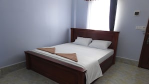 A neatly made bed with a wooden headboard, white bedding, and two brown towels.