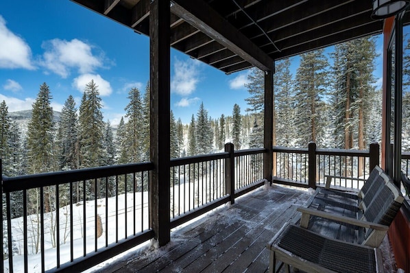 Una terraza de madera con vista a árboles nevados y un cielo despejado.