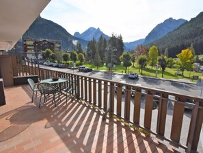 Ein Balkon mit Tisch und Stühlen, der auf eine Straße mit Autos und einen Park mit Bäumen und einem Spielplatz blickt.