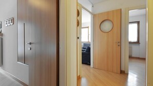 A modern interior with a wooden door, a round mirror, and a view into a living area with a sofa. - Condominio al Parco by Interhome (Canazei)