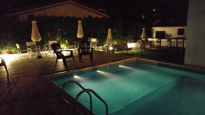 A swimming pool with lounge chairs and umbrellas, surrounded by a fence and a building. - Posada Mia Nonna (Villa General Belgrano)