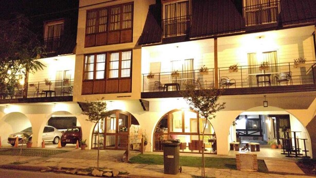 A multi-story hotel with a ground-level restaurant, outdoor seating, and a parking area. - Posada Mia Nonna (Villa General Belgrano)