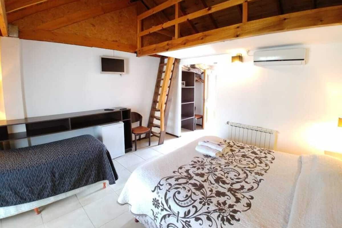 Um quarto com cama, escrivaninha, cadeira, escada e guarda-roupa.