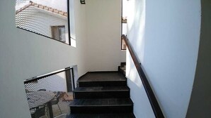 A staircase with black steps and a wooden handrail, leading to a landing with a mesh railing. - Posada Mia Nonna (Villa General Belgrano)