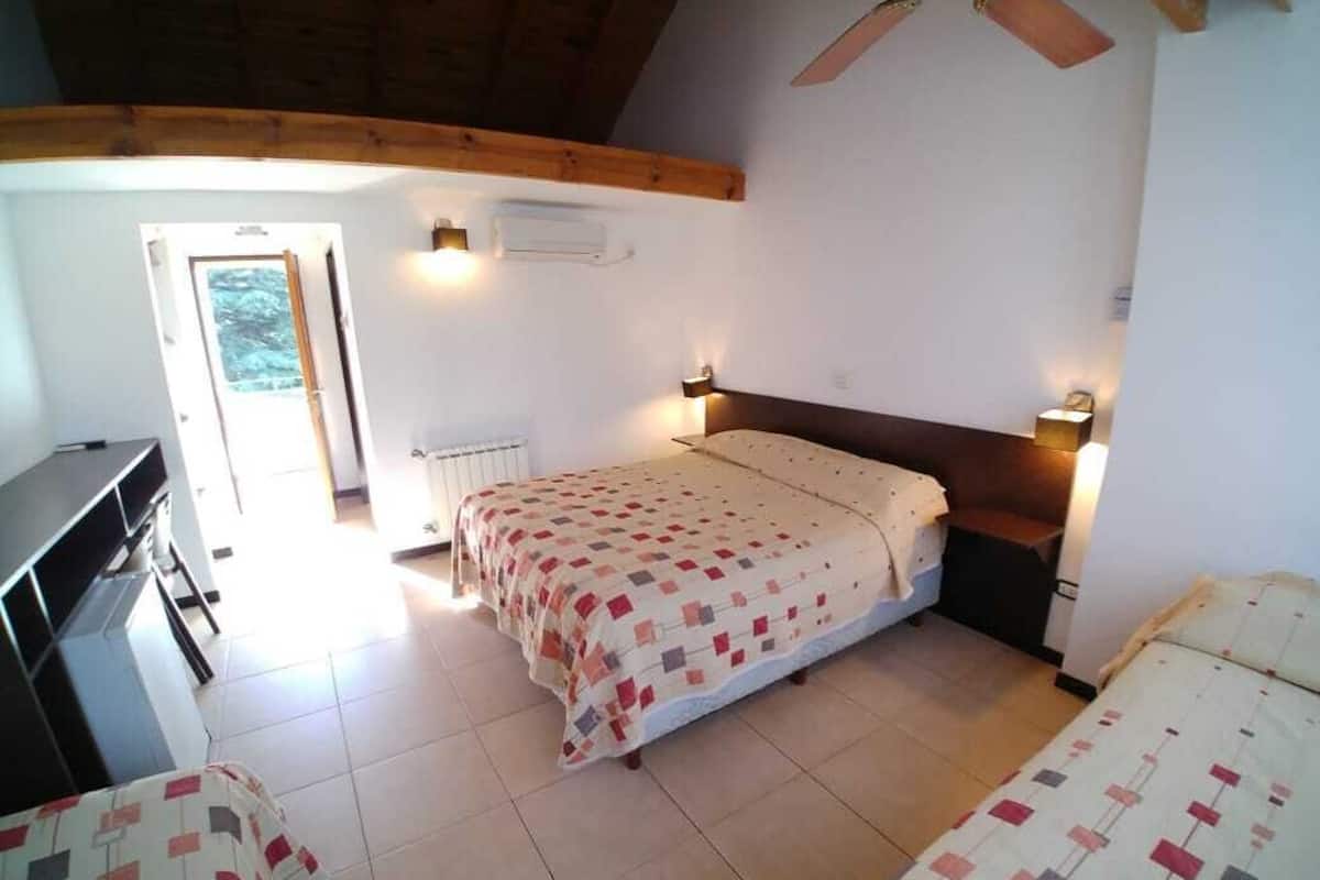 Quarto com uma cama, duas mesinhas de cabeceira, um radiador e um ventilador de teto.