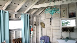 Um quarto rústico com teto de madeira, uma placa pendurada, uma cadeira rústica, uma mesa pequena e uma janela com cortinas.