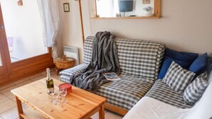 Een gezellige woonkamer met een geruit bankje, een houten tafel met een fles en glazen, en een spiegel aan de muur.