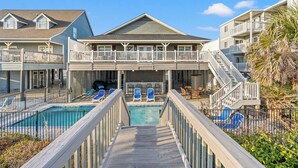 Ein Poolbereich mit Holzterrasse, die zu einem Pool führt, umgeben von Liegestühlen und einer überdachten Lounge.
