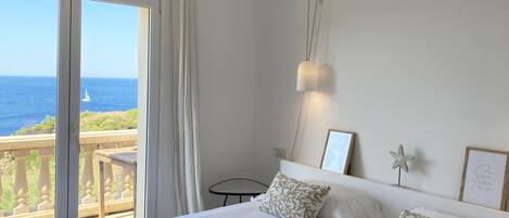 A bedroom with a large bed, a view of the sea, and a balcony.