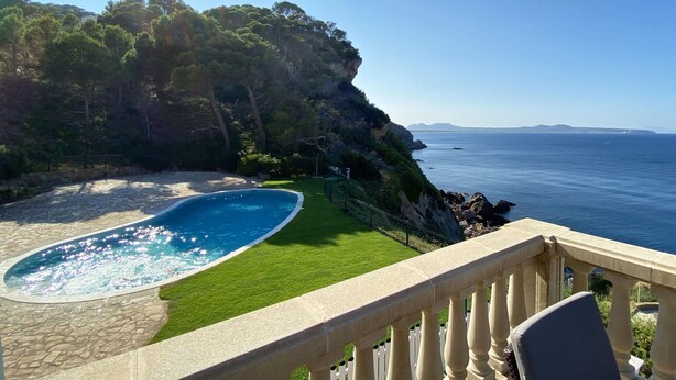 En pool med en kant av sten, en gräsyta och utsikt över havet och klipporna.