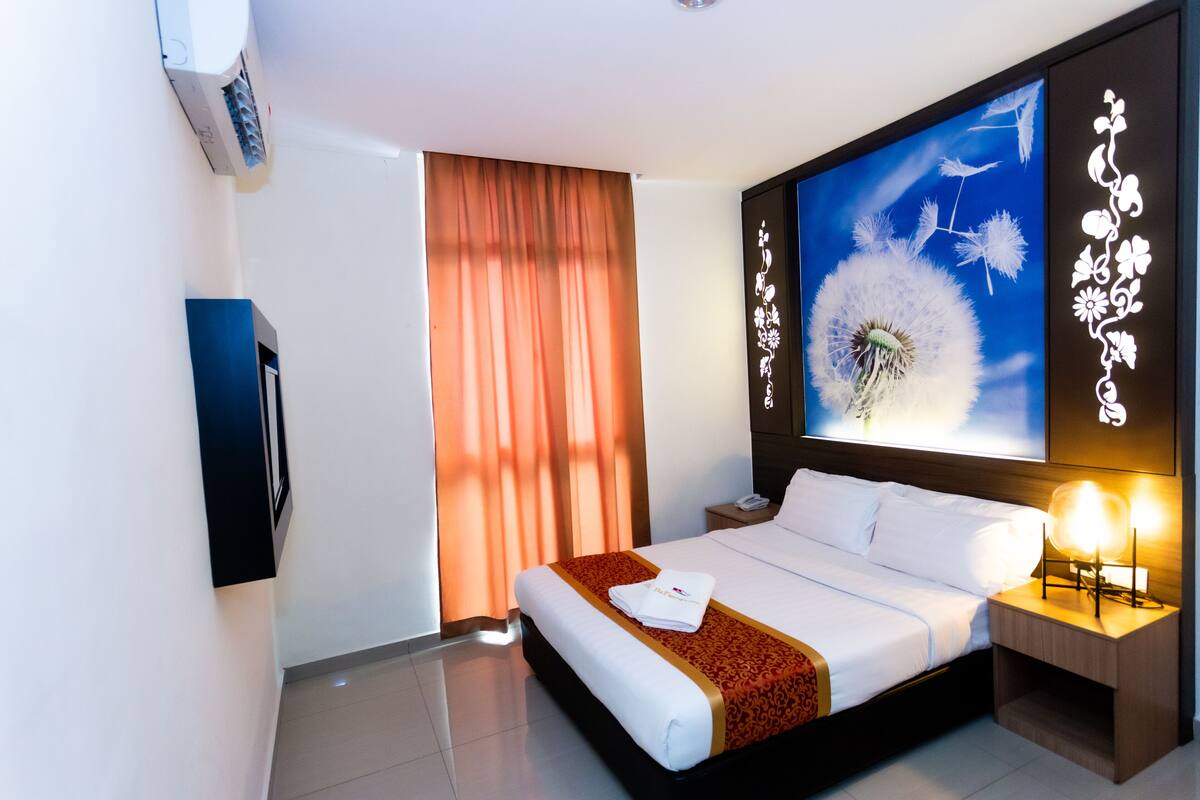 A modern hotel room with a large bed, a flat-screen TV mounted on the wall, and a large window with curtains.