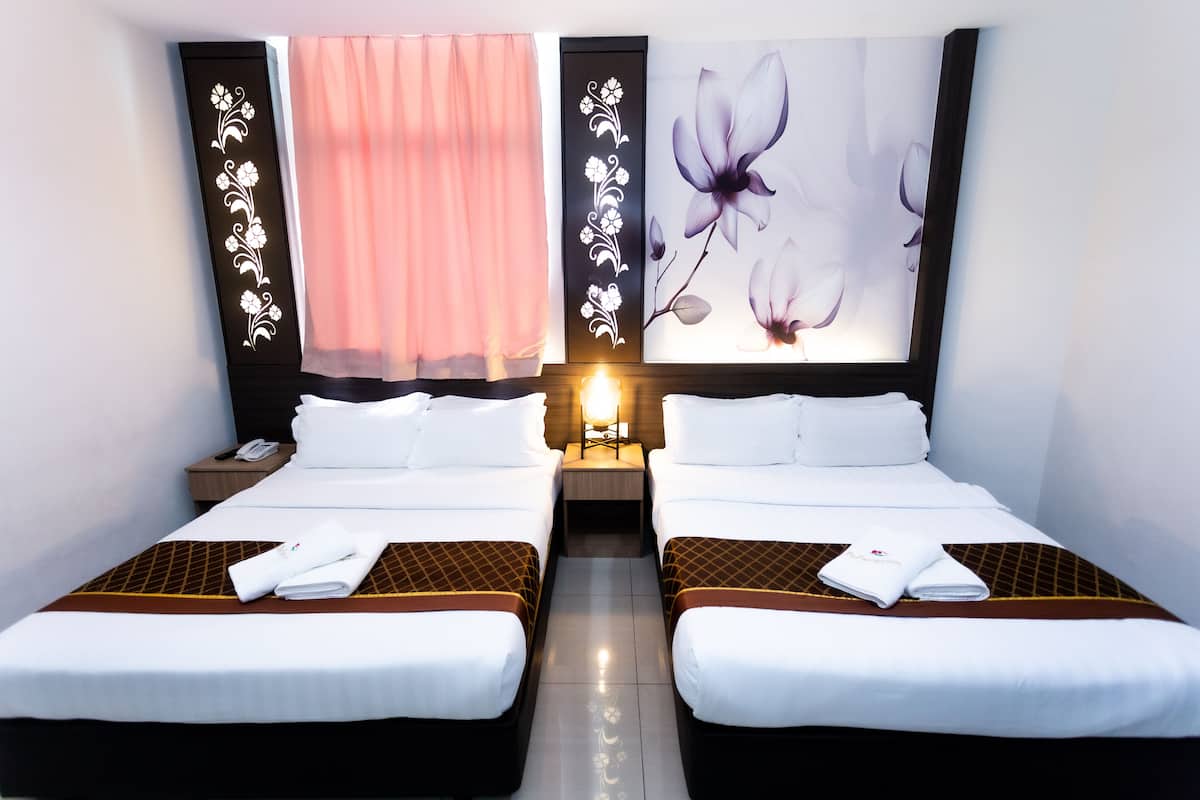 A hotel room with two beds, a nightstand with a phone, a wall-mounted lamp, and floral artwork on the wall.