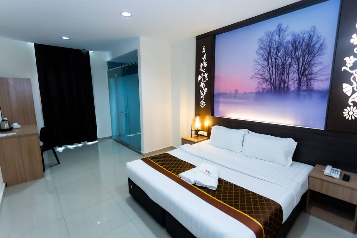 A hotel room with a large bed, a nightstand with a phone, a wall-mounted TV displaying a nature scene, and a separate bathroom with a glass door.