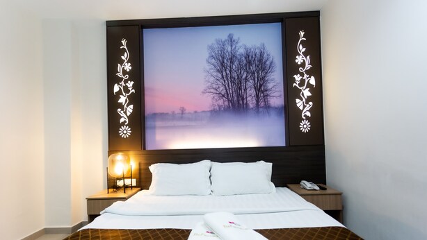 A hotel room with a large bed, a flat-screen TV mounted on the wall displaying a nature scene, a bedside table with a lamp, and a phone.
