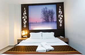 Habitación de hotel con una cama grande, un televisor de pantalla plana montado en la pared mostrando una escena natural, una mesita de noche con lámpara y un teléfono.