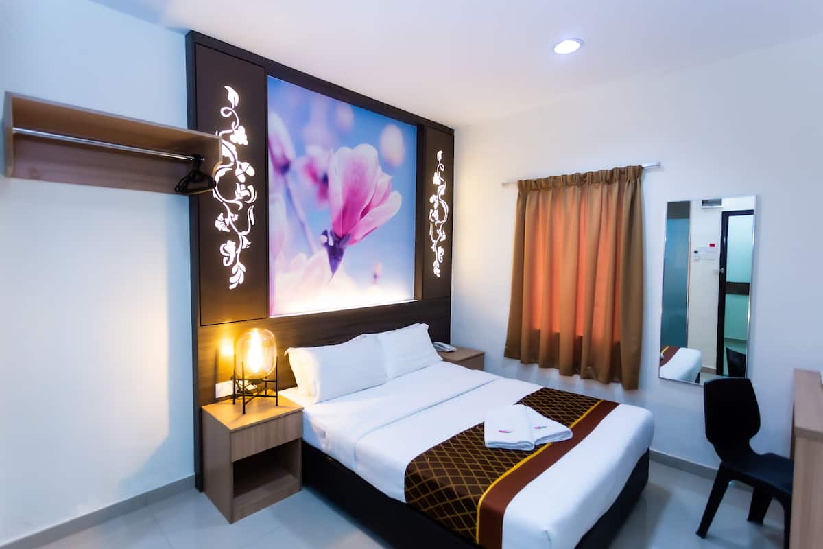 A hotel room with a large bed, a bedside table with a lamp, a mirror, and a window with curtains.