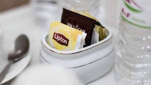 A white ceramic bowl containing Lipton tea bags and a chocolate packet, placed on a white table next to a clear plastic bottle.