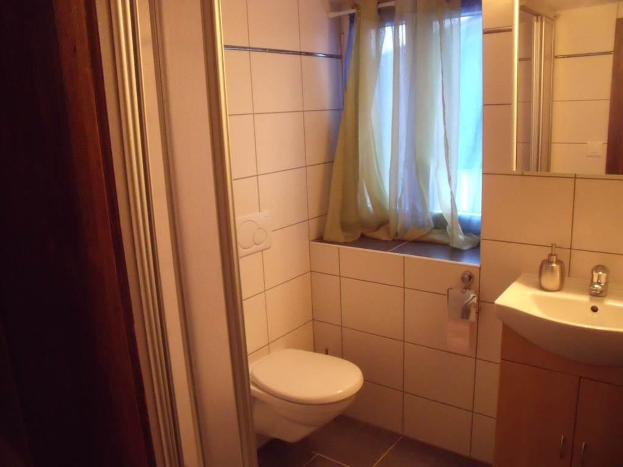A small bathroom with a toilet, a sink, and a window with a curtain.