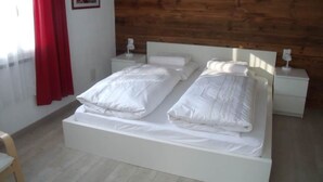 Un lit double avec une literie blanche, deux tables de chevet, une tête de lit en bois et un rideau rouge.