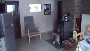 Un espace de vie compact comprenant un coin cuisine, un fauteuil gris, un petit tabouret et une cheminée.