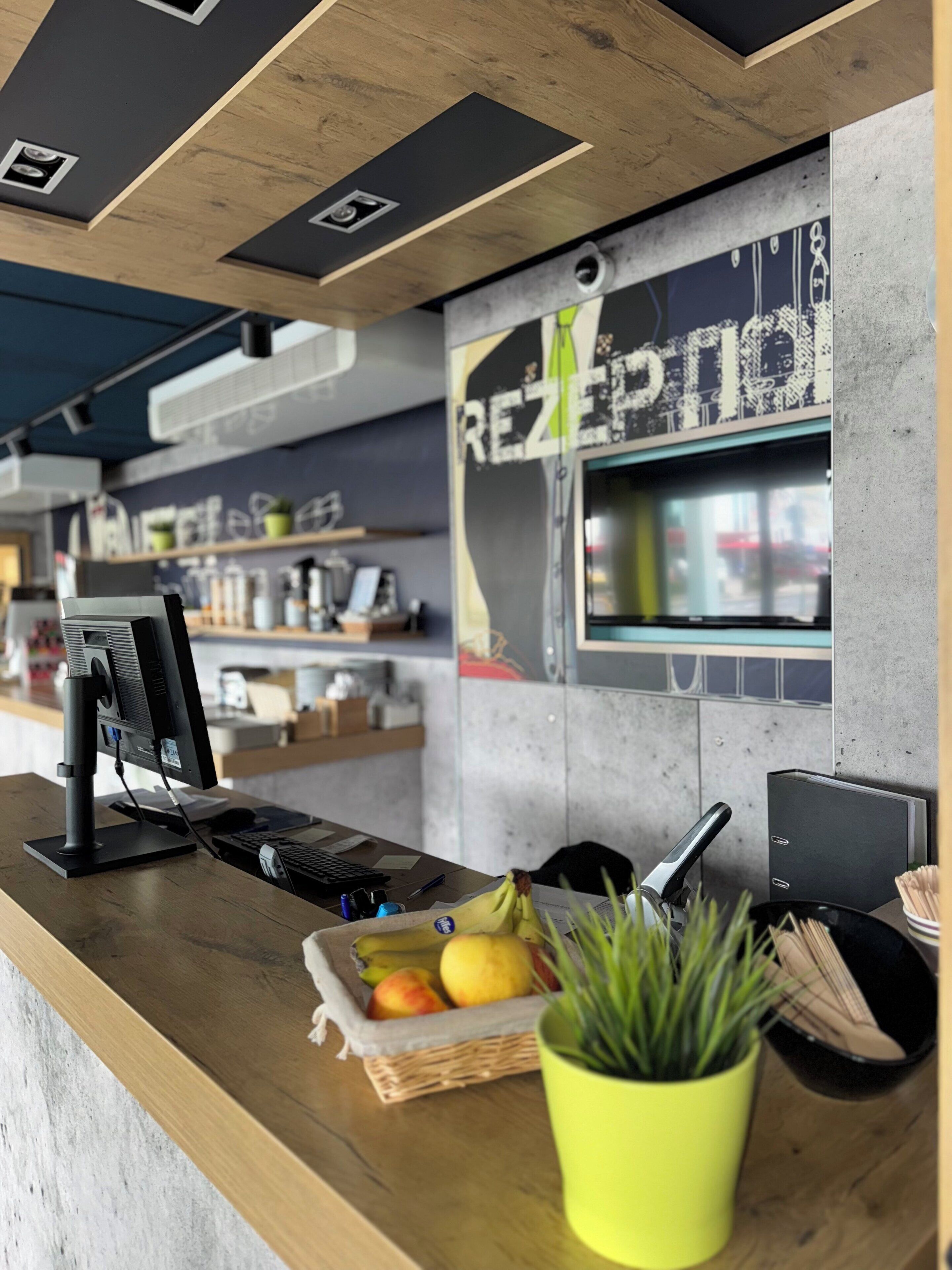 A counter with a computer, a cash register, and a basket of fruit.