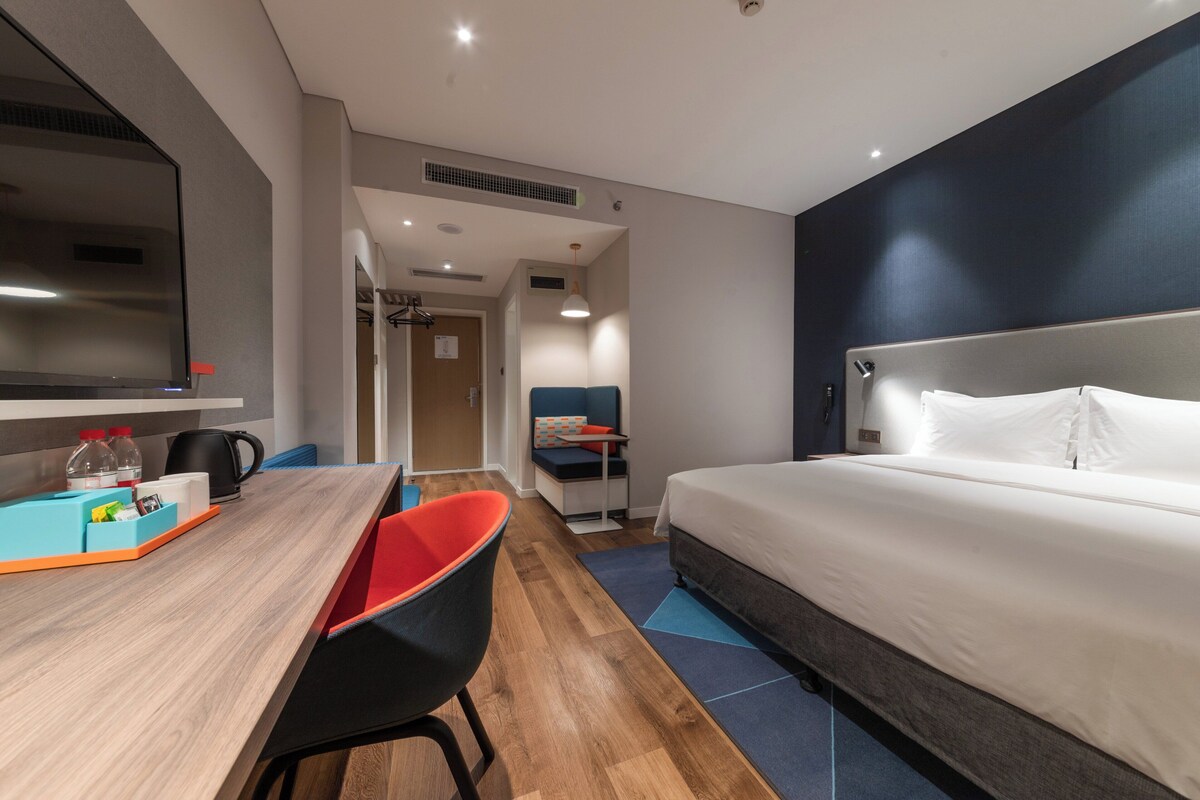 A hotel room with a bed, a desk with a chair, a television, and a kitchenette area.