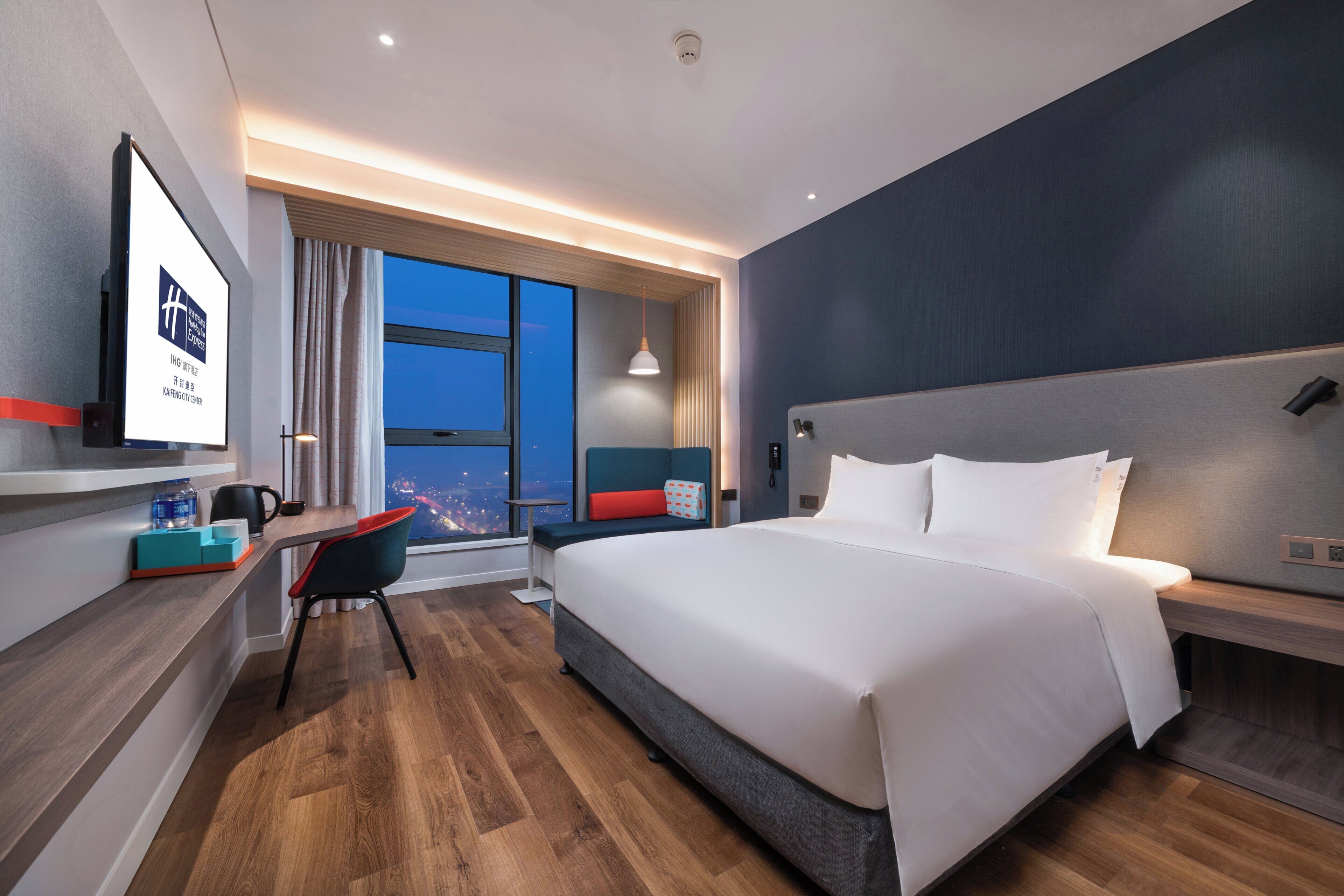 Habitación de hotel moderna con una cama grande, un escritorio con silla, un ventanal y vistas a la ciudad.