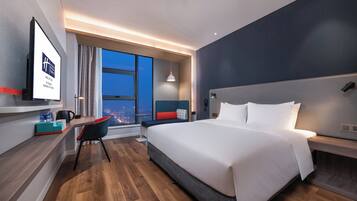 Habitación de hotel moderna con una cama grande, un escritorio con silla, un ventanal y vistas a la ciudad.