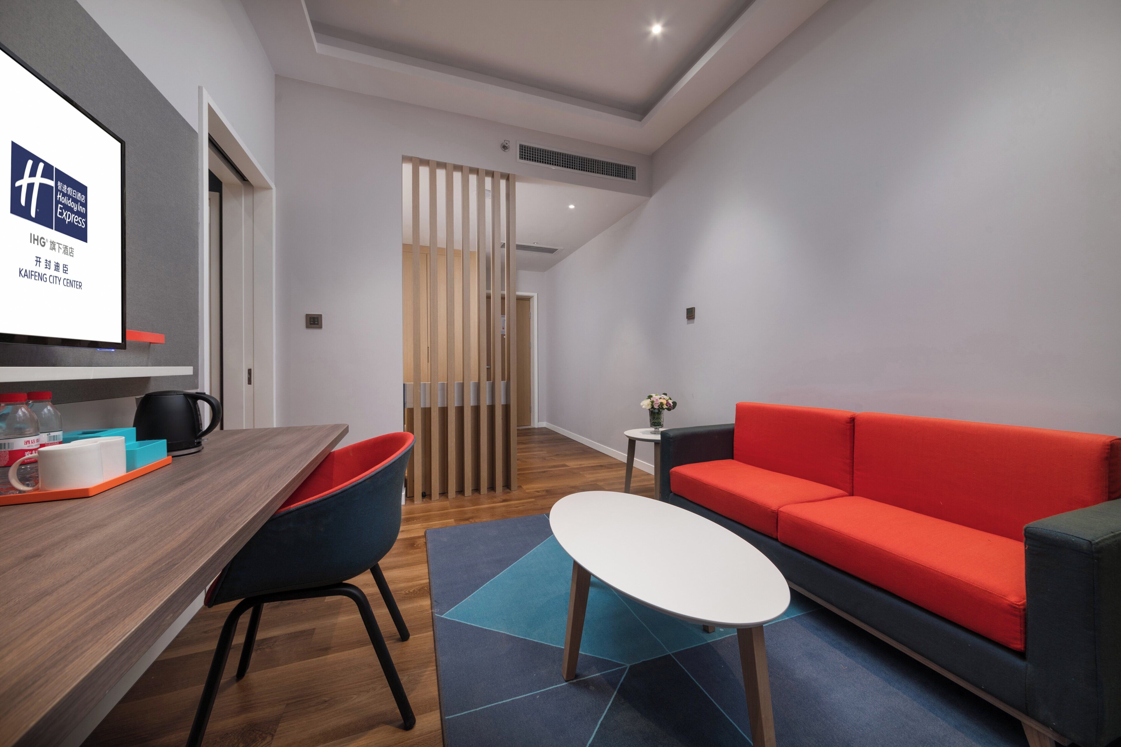A modern hotel room with a wooden desk, a red sofa, and a small white table.