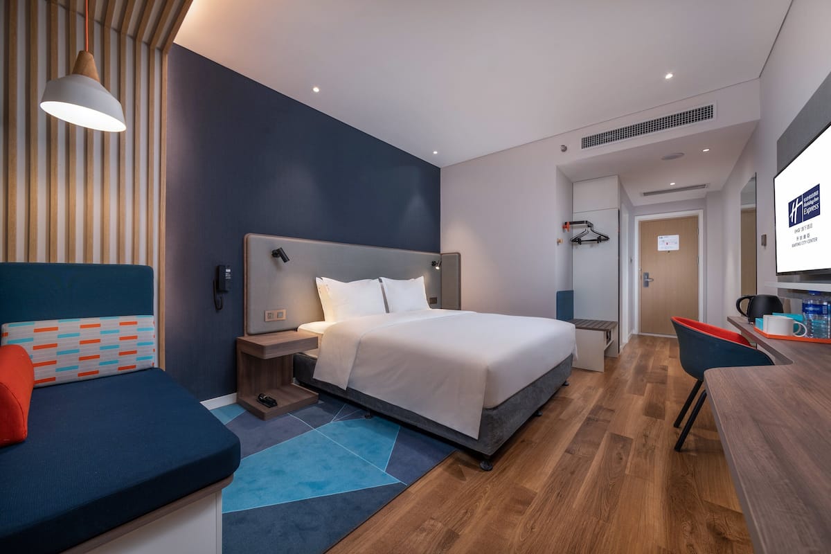 A modern hotel room with a bed, bedside table, and a desk with a chair.