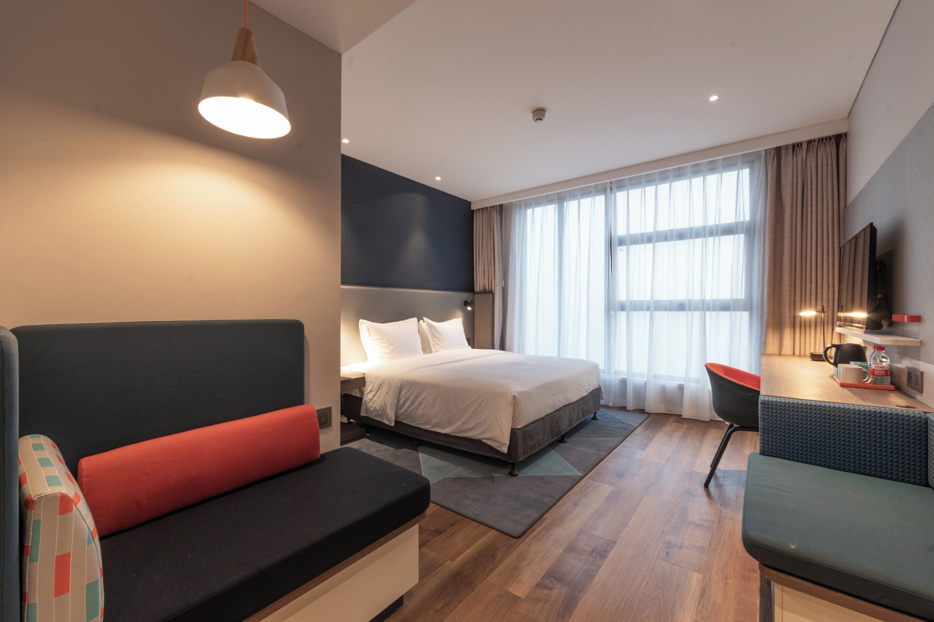 Una habitación de hotel moderna con una cama, un sofá, un escritorio y un televisor.