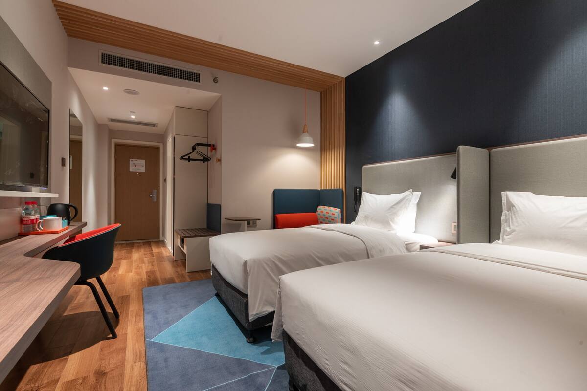 A hotel room with two beds, a desk, a chair, a small table, and a blue rug.