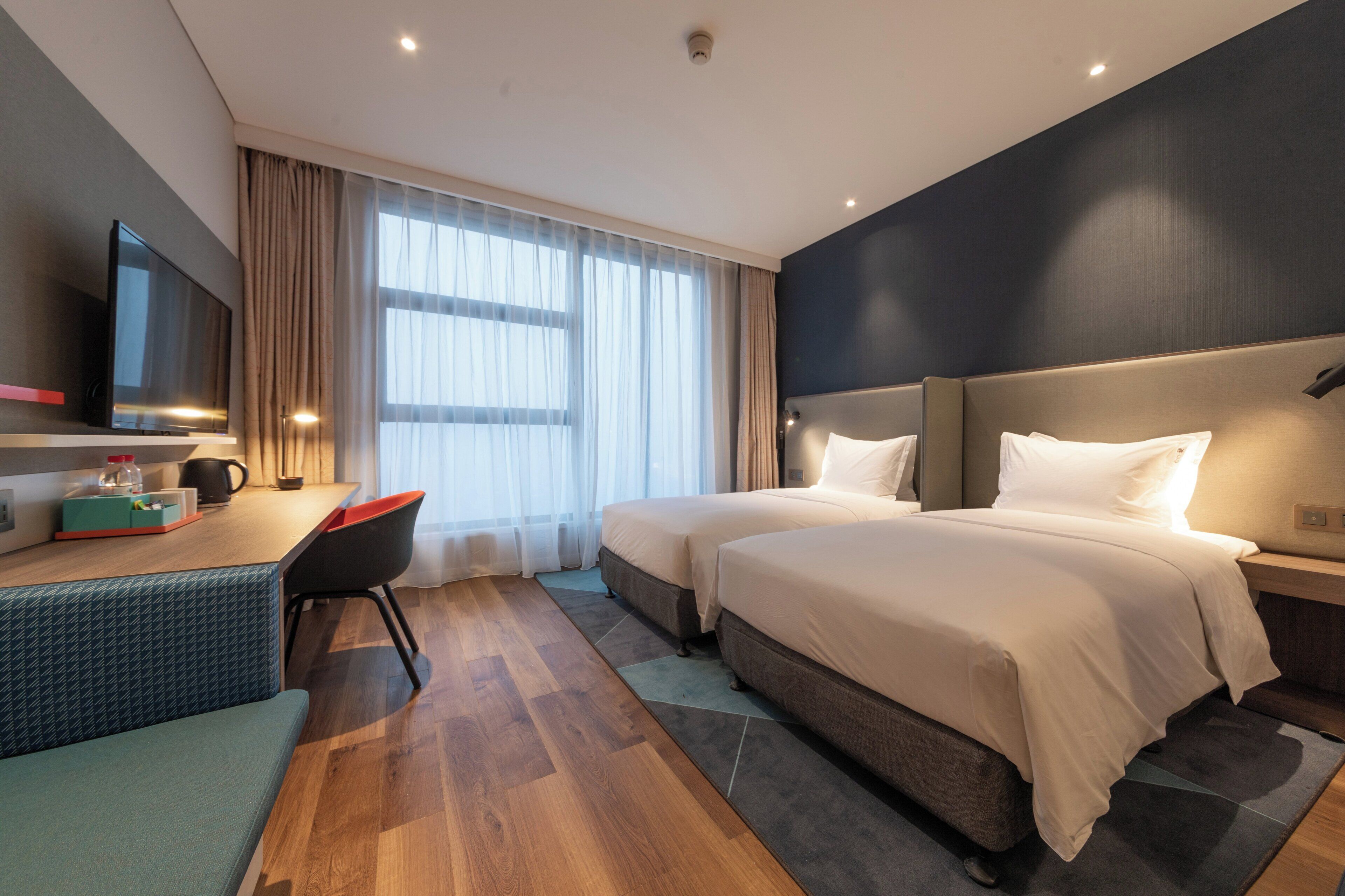Een hotelkamer met twee bedden, een bureau, een stoel, een televisie en een raam met gordijnen.