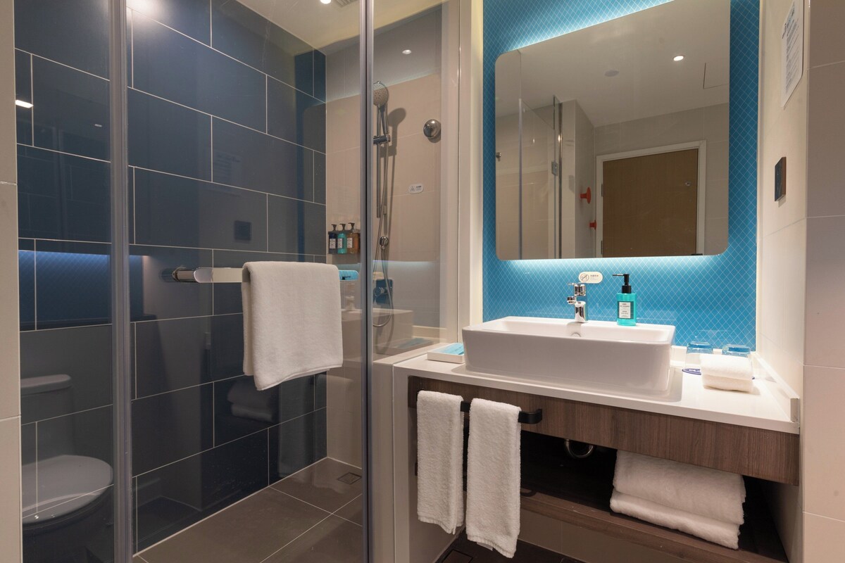 A modern bathroom with a glass shower enclosure, a white sink, and a mirror with a blue accent wall.