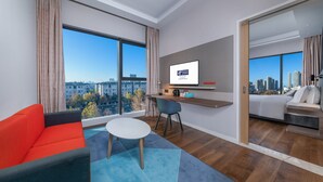 A modern hotel room with a large window, a sofa, a small table, and a bed.