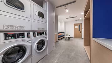 A laundry room with multiple washing machines, a blue wall, and a door leading to another room.