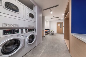A laundry room with multiple washing machines, a blue wall, and a door leading to another room.