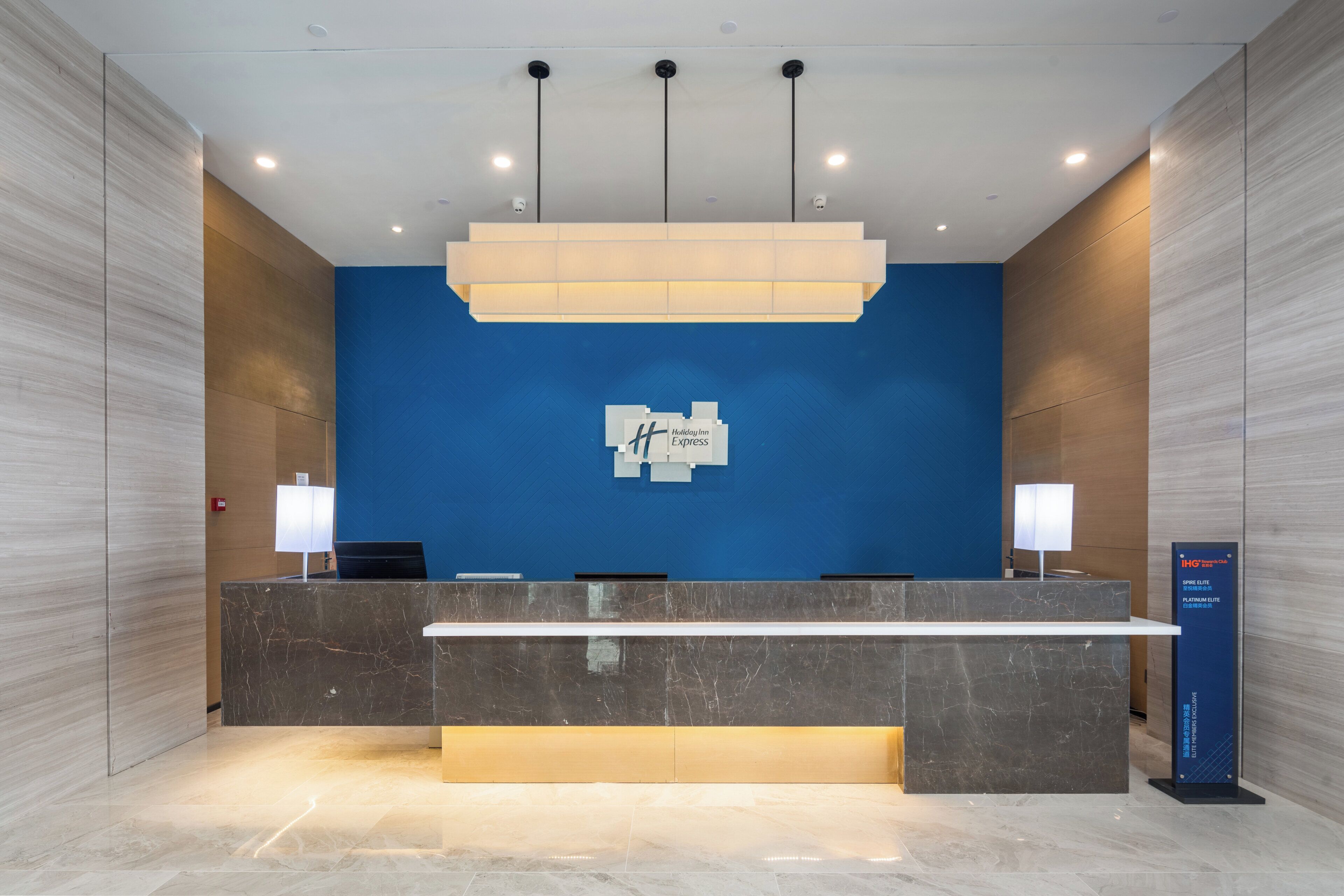 A hotel reception desk with a blue wall, a marble counter, and a sign indicating the Holiday Inn Express.