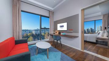 Une chambre d’hôtel moderne dotée d’une grande fenêtre, d’un canapé, d’une petite table, d’un bureau avec un ordinateur et d’un lit.
