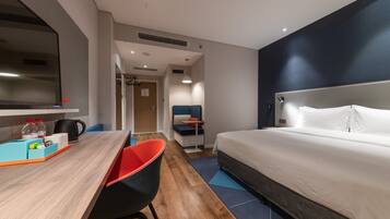 Habitación de hotel con cama, escritorio y silla, televisor y una pequeña cocina.