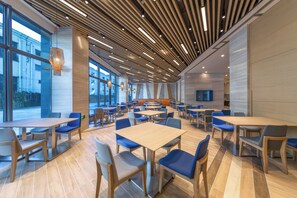 A modern dining area with wooden tables and chairs, large windows, and a slatted ceiling design. - Holiday Inn Express Kaifeng City Center by IHG (Kaifeng)