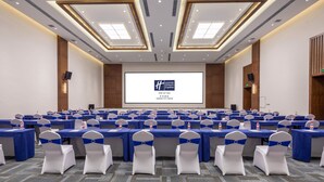 A conference room with multiple tables and chairs, a large screen at the front, and a modern ceiling design.
