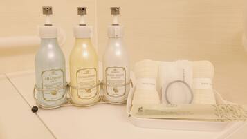 A bathroom with three bottles of shampoo, conditioner, and body wash, and a set of towels and a toothbrush.