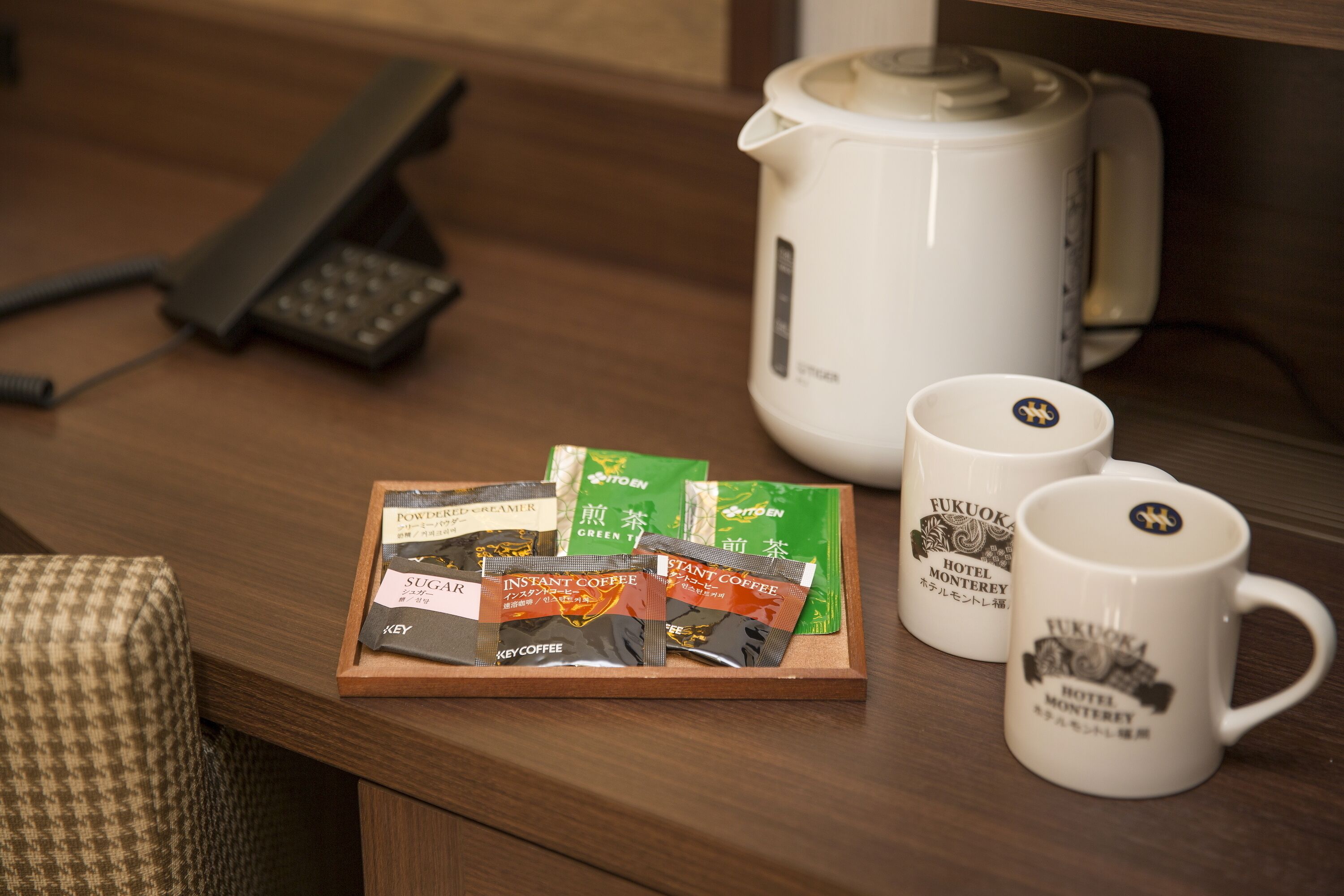 A wooden tray with instant coffee packets and two white mugs with a hotel logo.