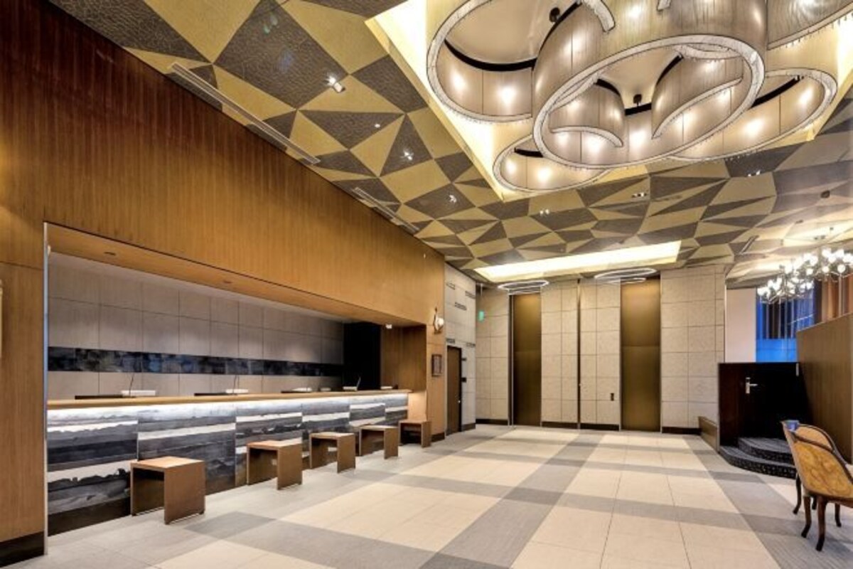 A hotel lobby with a check-in counter, seating area, and a patterned ceiling.