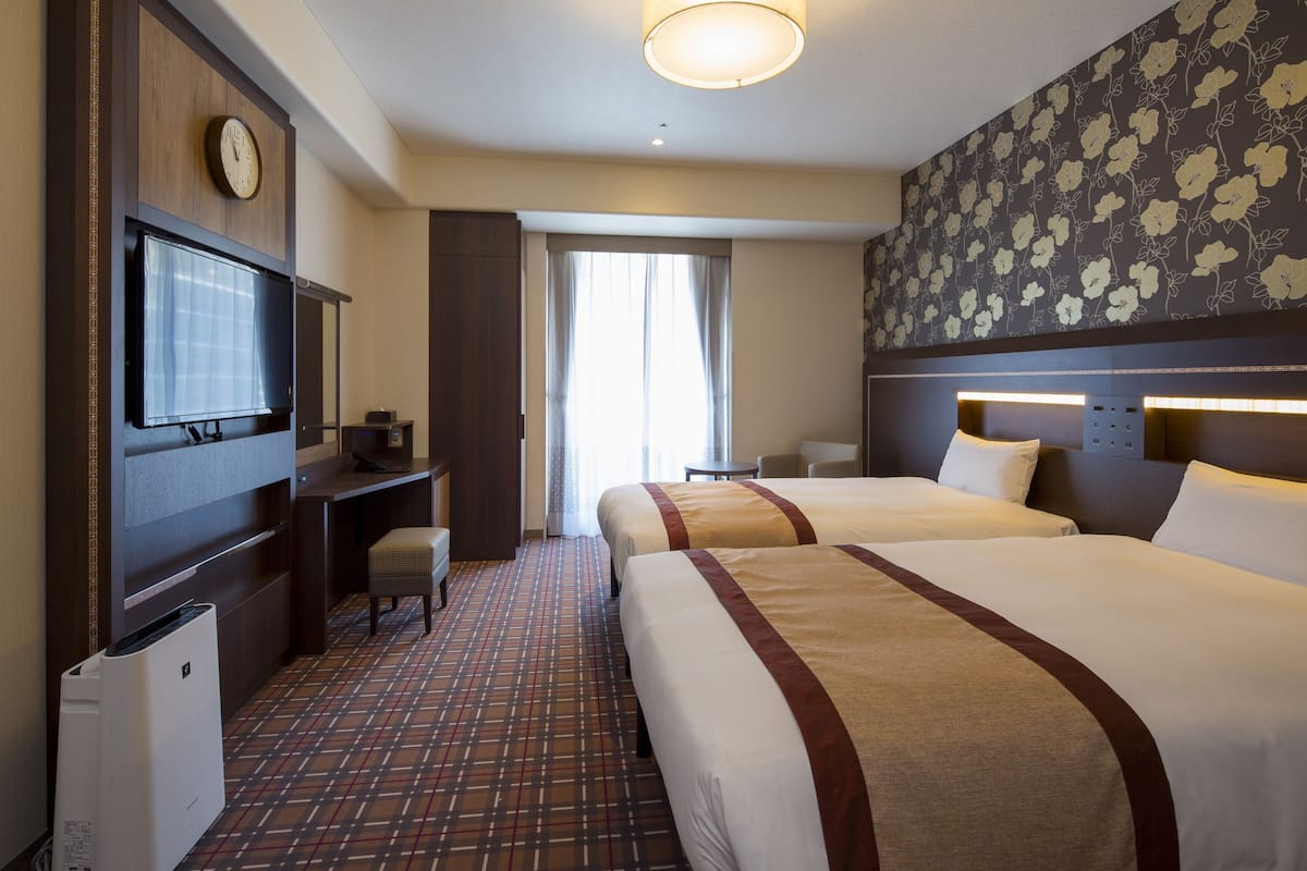 Habitación de hotel con dos camas, televisión, escritorio y un ventanal grande.