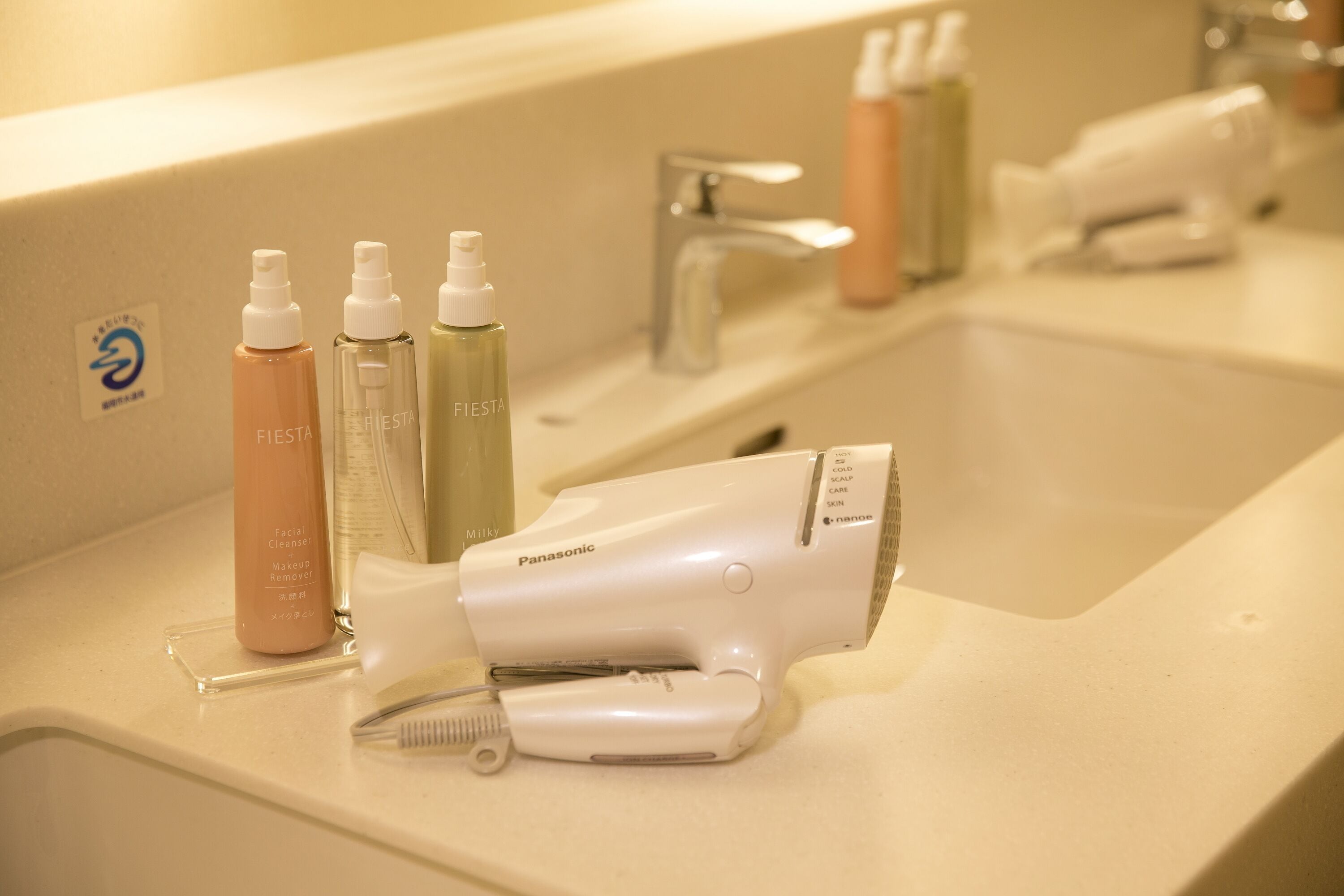 Ein Badezimmer mit Waschbecken, Fön und verschiedenen Hautpflegeprodukten.