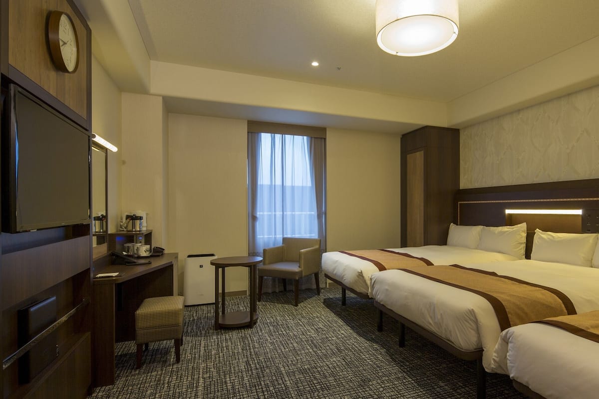 Una habitación de hotel con cama, escritorio, silla, televisor y ventana con cortinas.