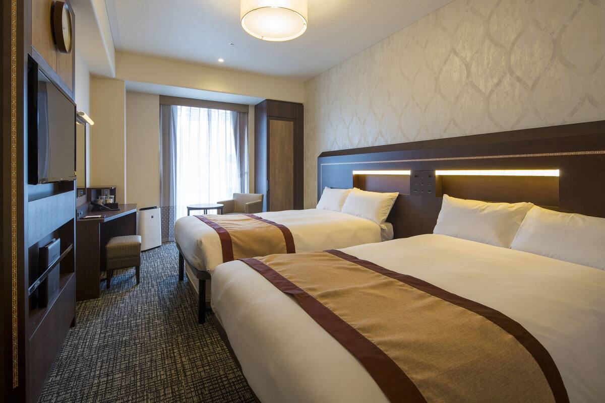 Una habitación de hotel con dos camas, un escritorio, una silla y una mesita.